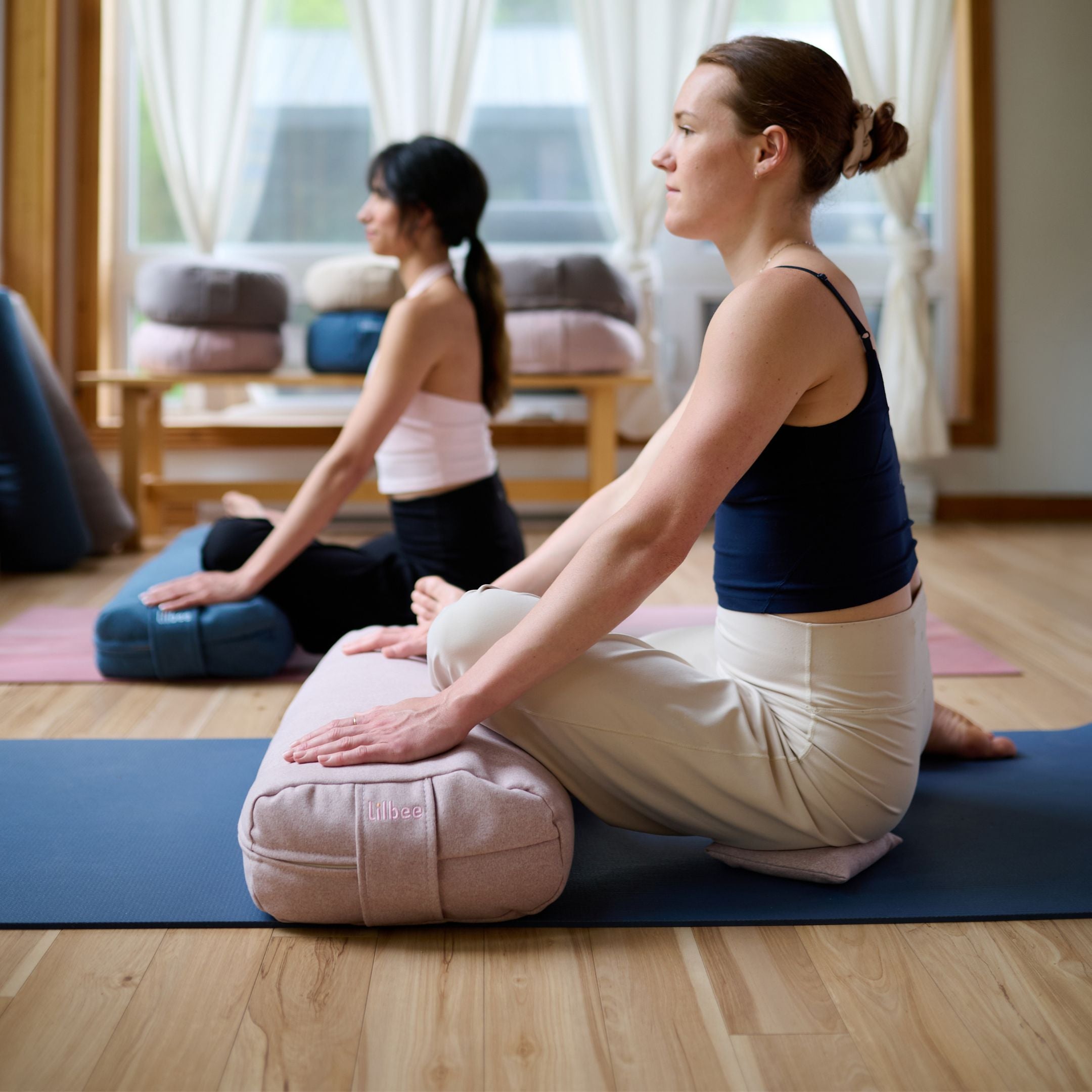 Two women practicing yoga indoors with Lilbee meditation cushions in a calm, bright studio space.