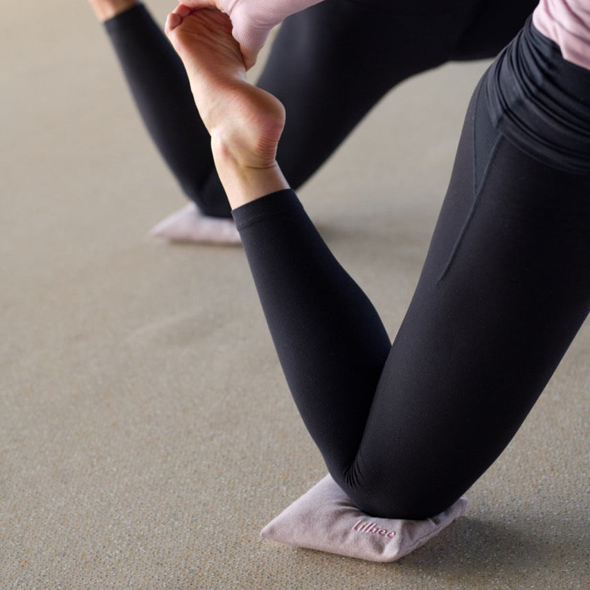 Close-up of yoga practitioners using Lilbee knee pads for support during a low lunge. Soft, eco-friendly padding protects knees on hard floors, handcrafted in Canada from recycled materials.