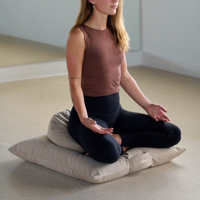 Woman meditating cross-legged on a Lilbee zabuton floor cushion in a calm studio. Thick, supportive base handmade in Canada from recycled fabrics for enhanced comfort and grounding.