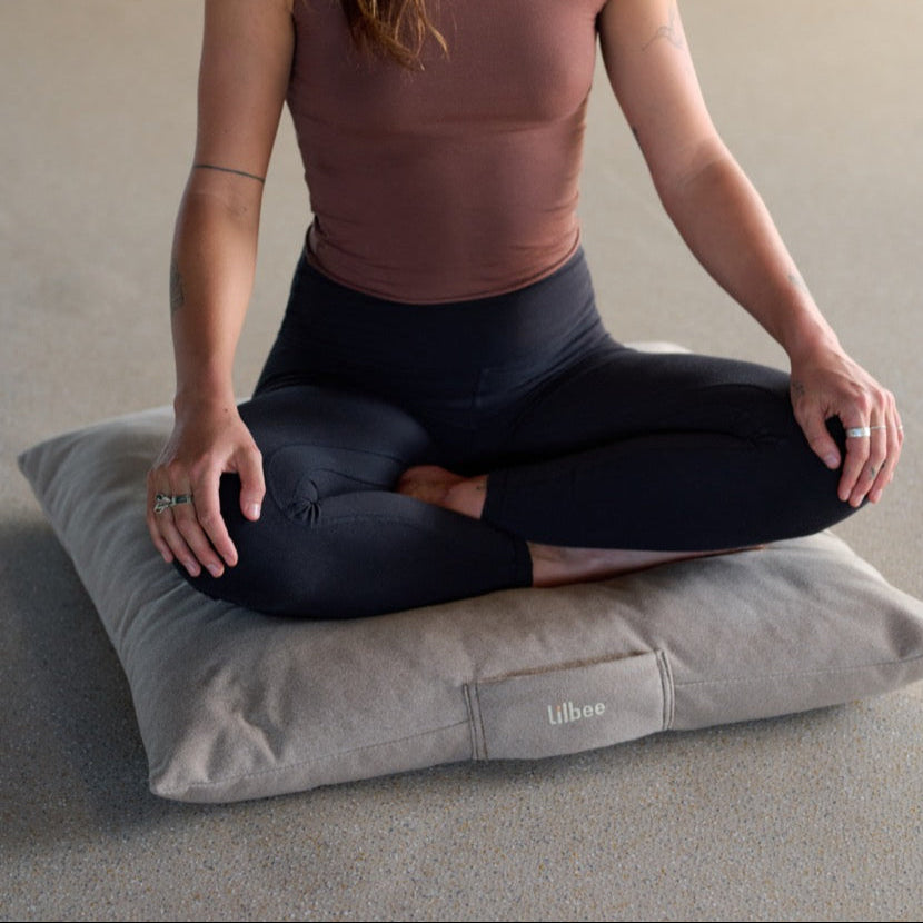 Woman seated in lotus pose on a grey Lilbee zabuton cushion. Eco-friendly meditation mat made in Canada with recycled textile filling for lasting comfort and mindful grounding.