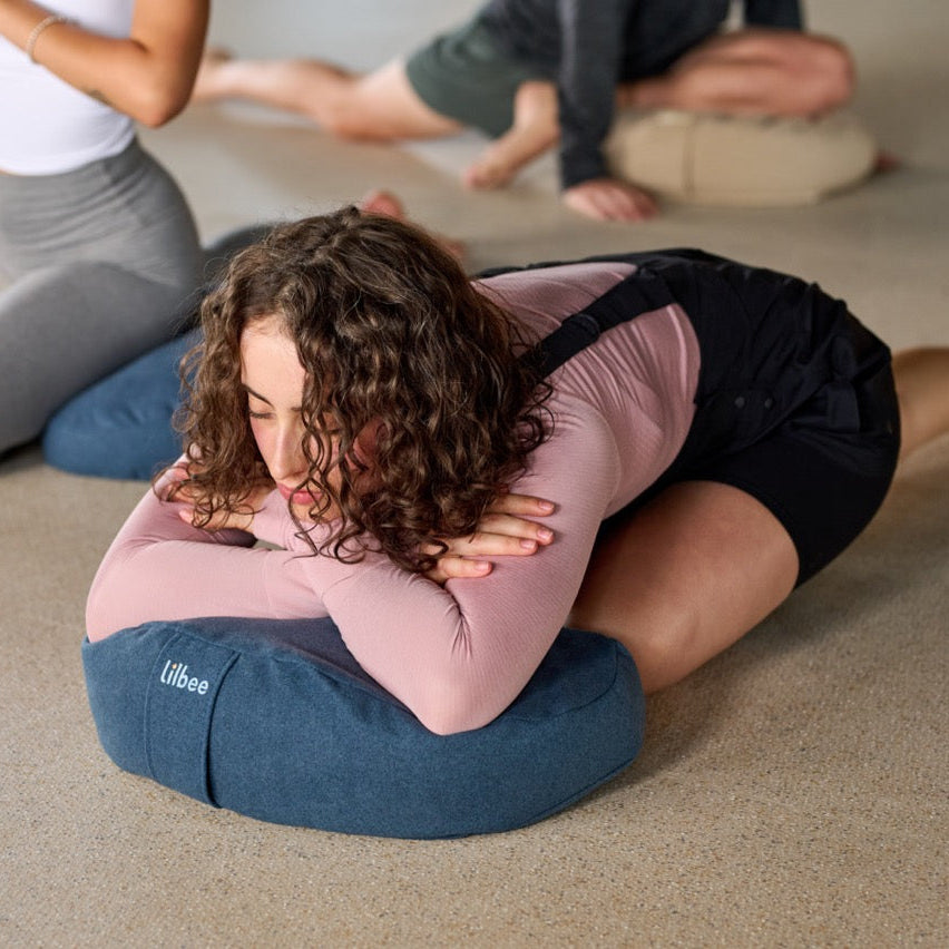 Woman resting forward on a blue Lilbee crescent cushion for meditation and yoga. Sustainable design handcrafted in Canada with soft recycled-textile filling for optimal comfort.